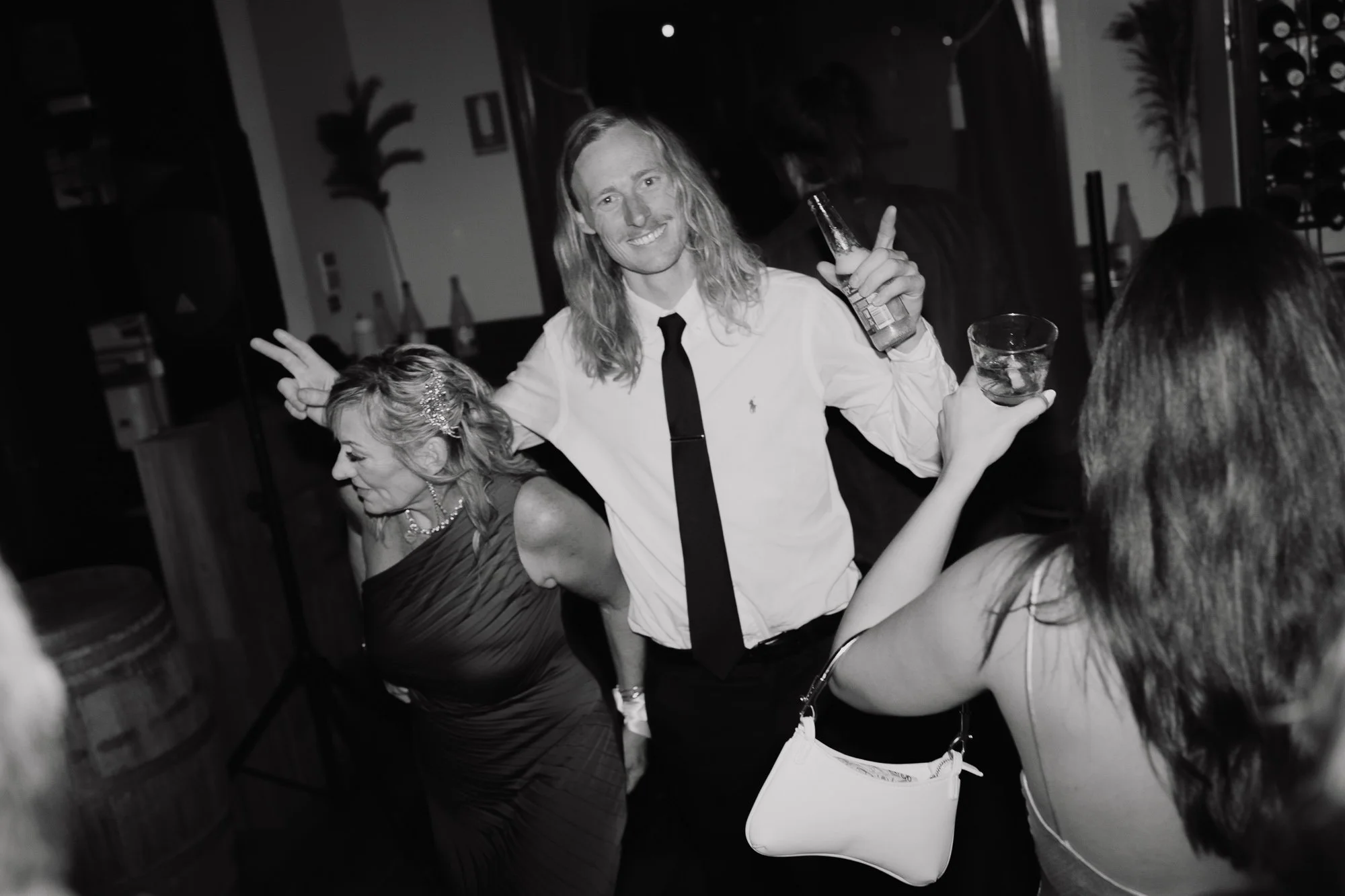 A group of people dancing and enjoying a wedding reception at Boho South Wharf, with one person holding a drink and making a peace sign gesture.