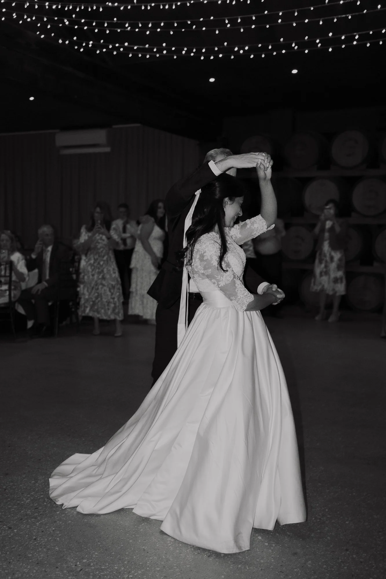 A black and white photo of a bride and groom dancing at a wedding reception at Witchmount Estate, with guests in the background enjoying the event.