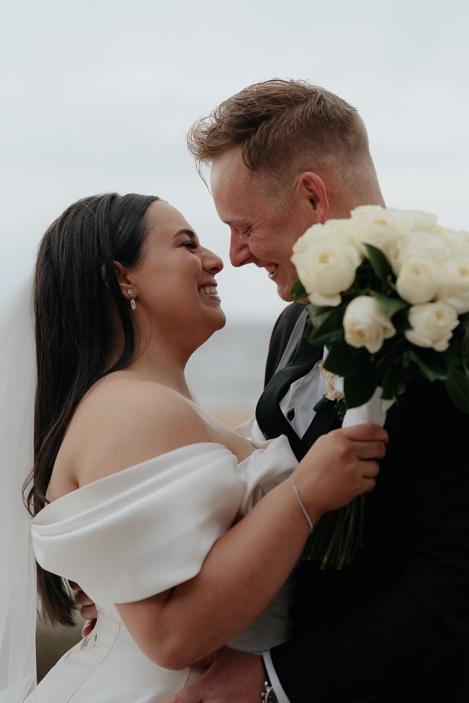 Melbourne Beach Wedding Photography. Whitestone Events. Bride and Groom laughing at beach, holding white roses.