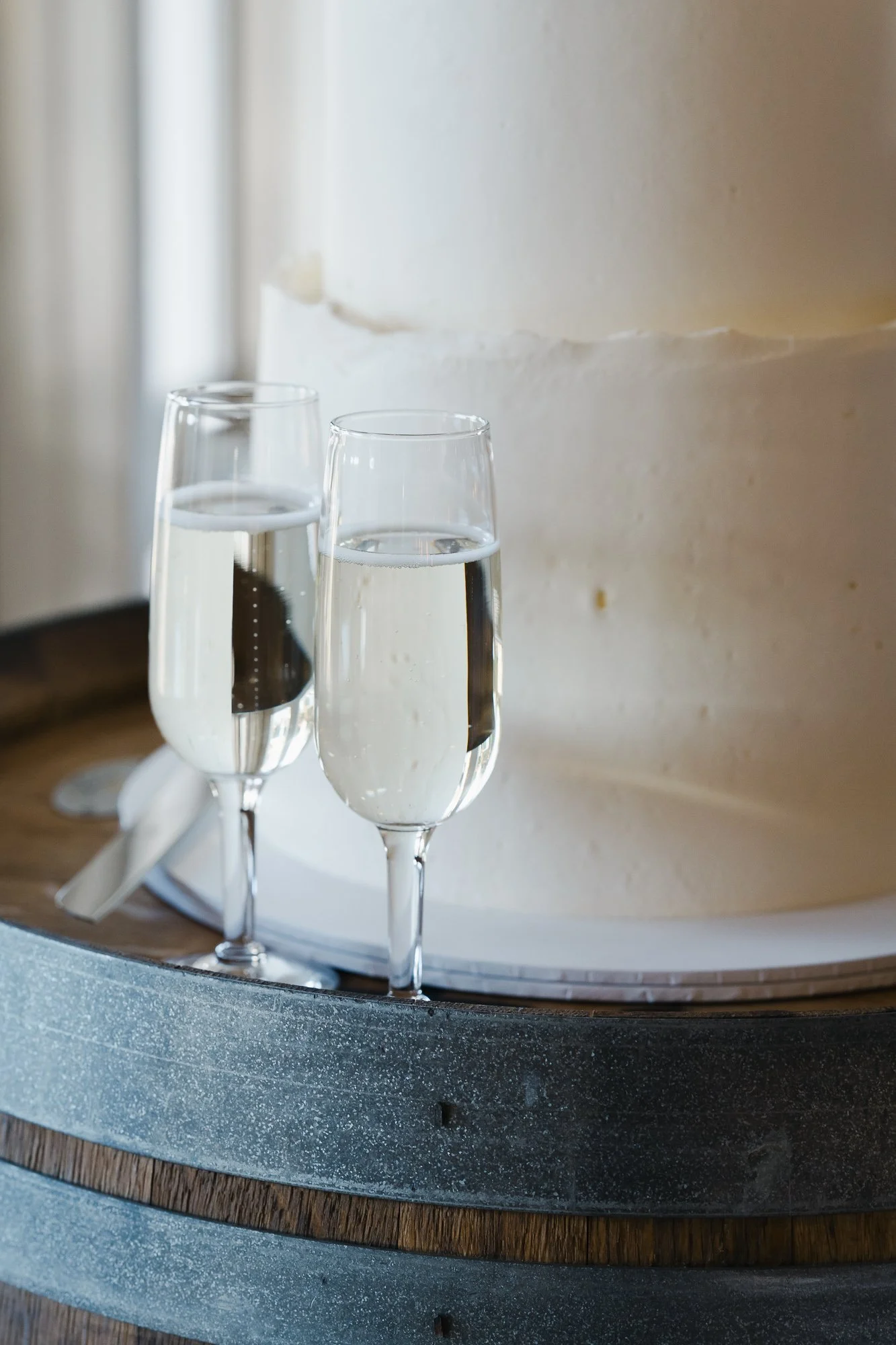 Two glasses of champagne on a barrel next to a white wedding cake.