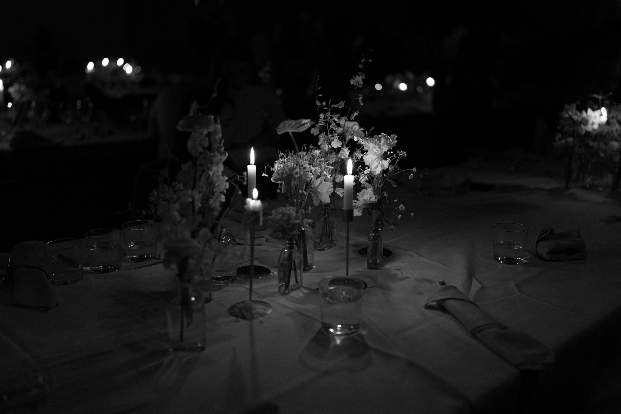 A table set with candles, glasses of water, and floral centerpieces at a nighttime event. Half Acre South Melbourne Wedding.