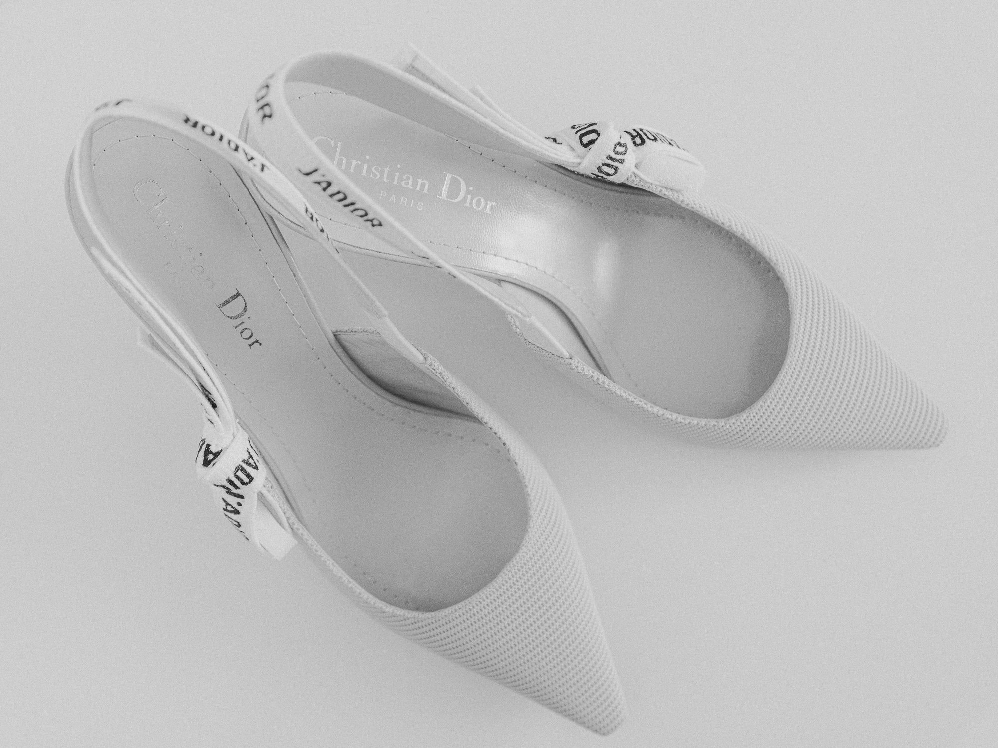 A pair of white Christian Dior high heels with pointed toes, viewed from above on a plain surface.