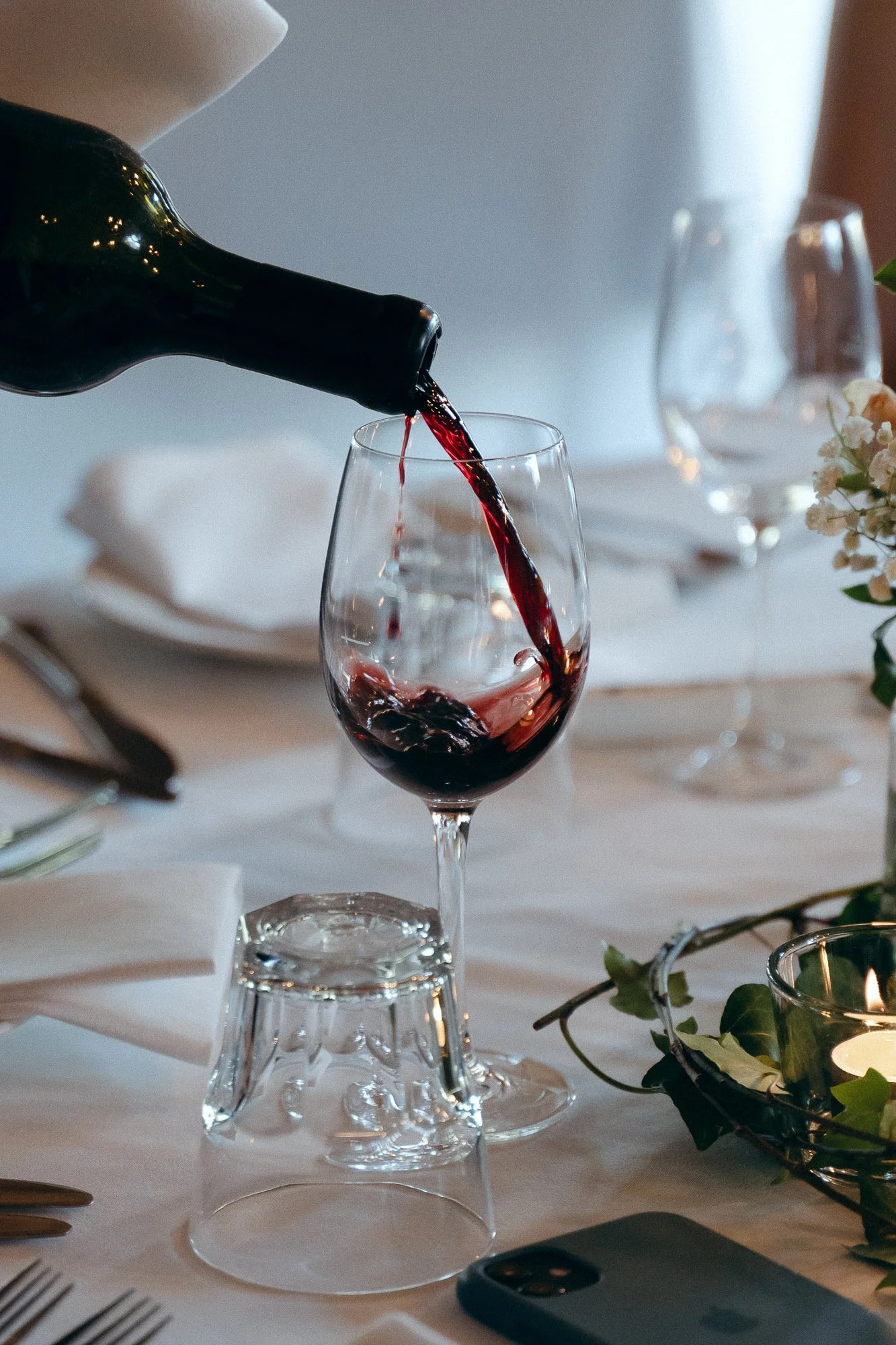 Red wine being poured into a wine glass on a table set for a meal.