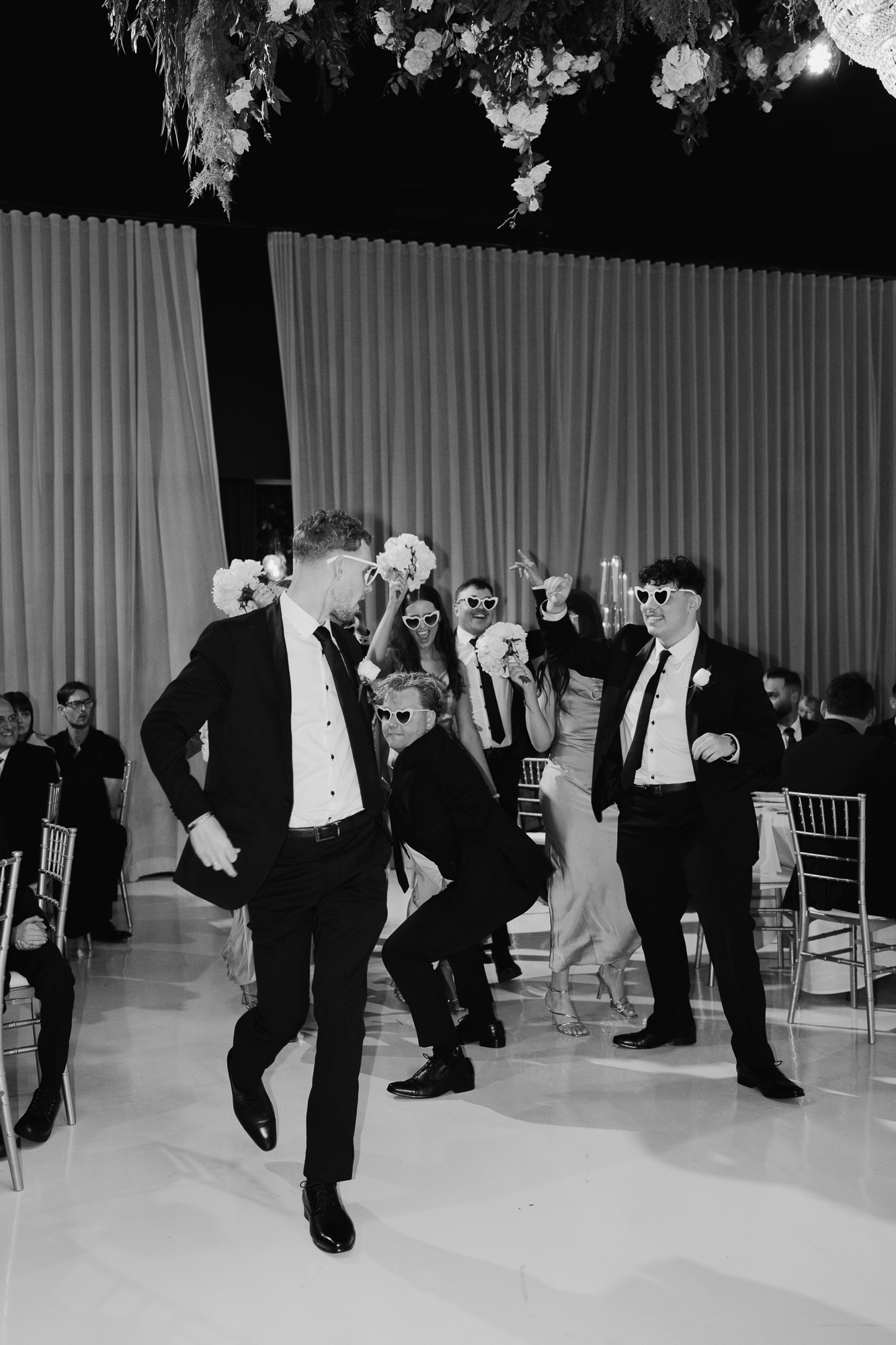 People at a wedding reception dancing and having fun, wearing sunglasses and formal attire. Whitestone Events Wedding Reception