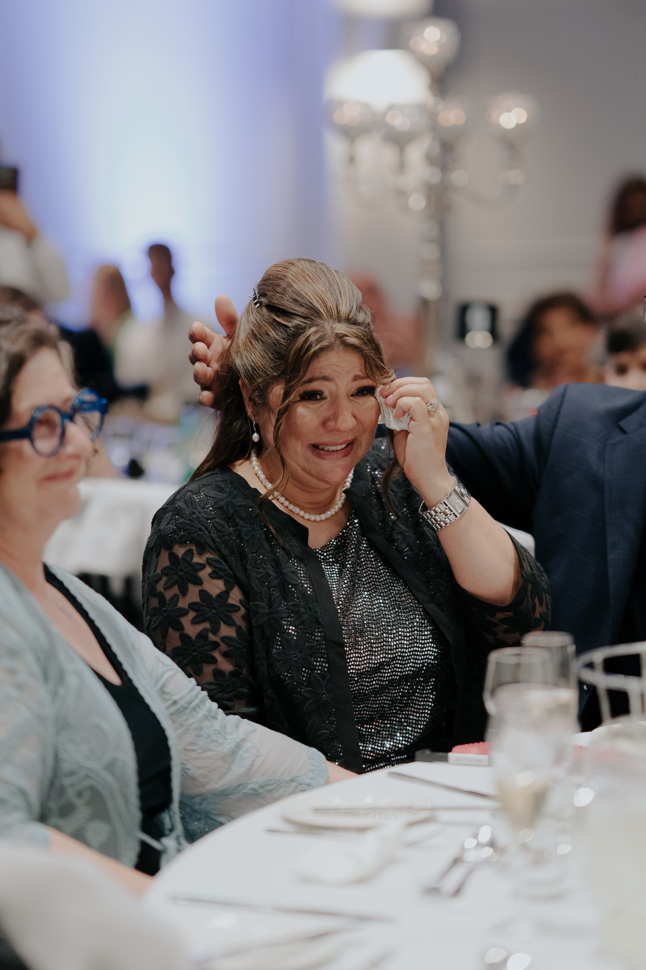 A woman at a formal event, crying and wiping tears from her eyes, sitting at a table with other guests. Lakeside Events