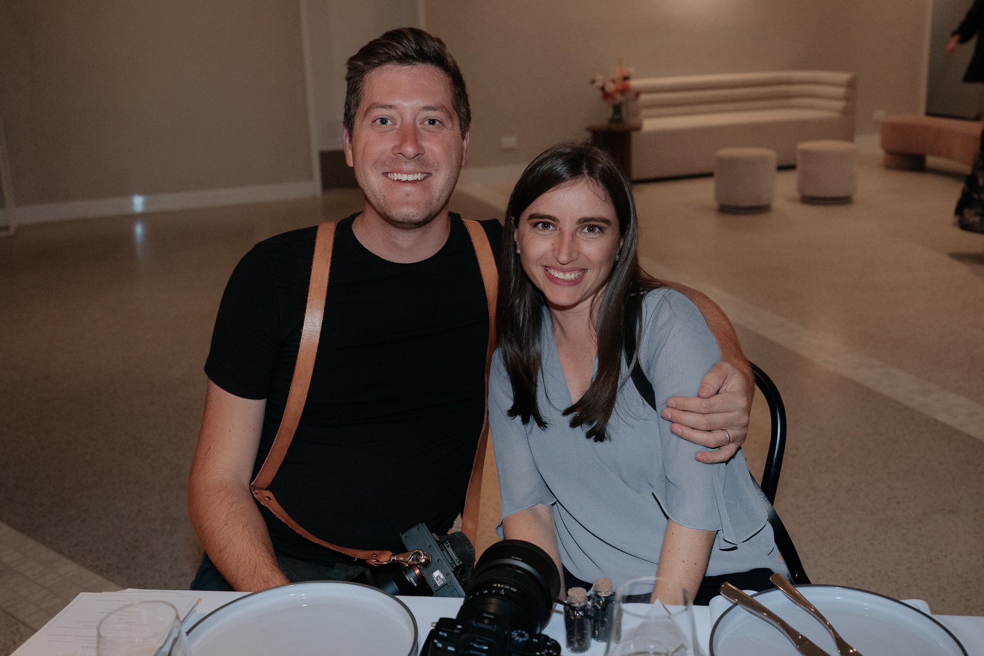 A man and woman smiling and sitting at a table with plates, utensils, and cameras at The Terrace, Melbourne Botanical Gardens
