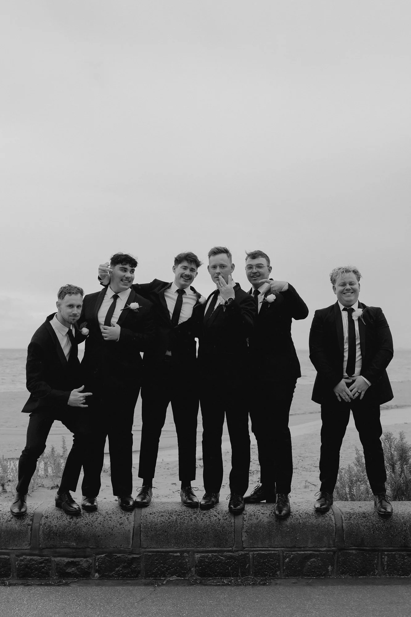 Group of six men in suits and ties standing on a concrete ledge on a beach