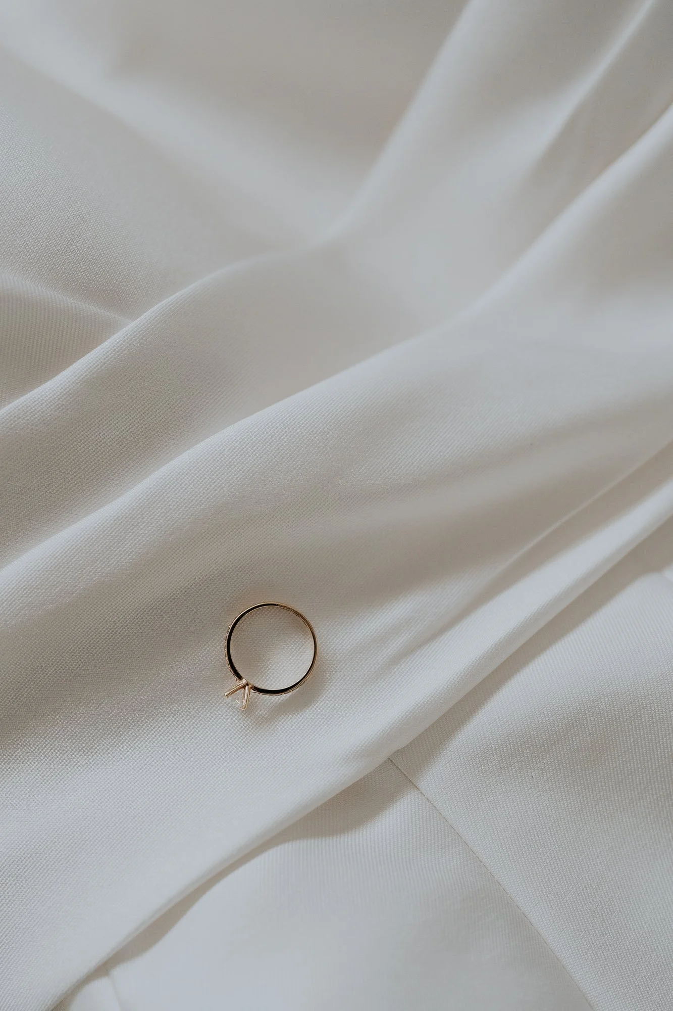 A close-up of a delicate ring with a small bow on a cream-colored fabric surface.