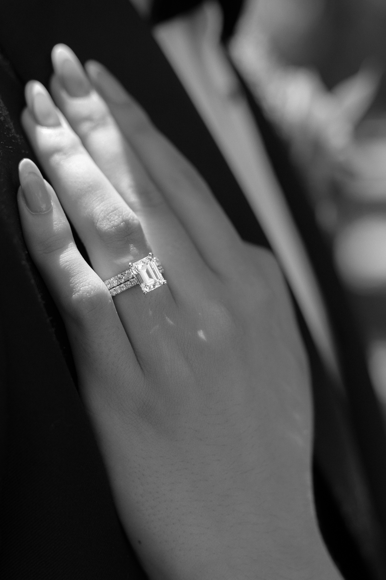 Close-up of a woman’s hand wearing an engagement ring with a large emerald-cut diamond and a diamond-studded band.