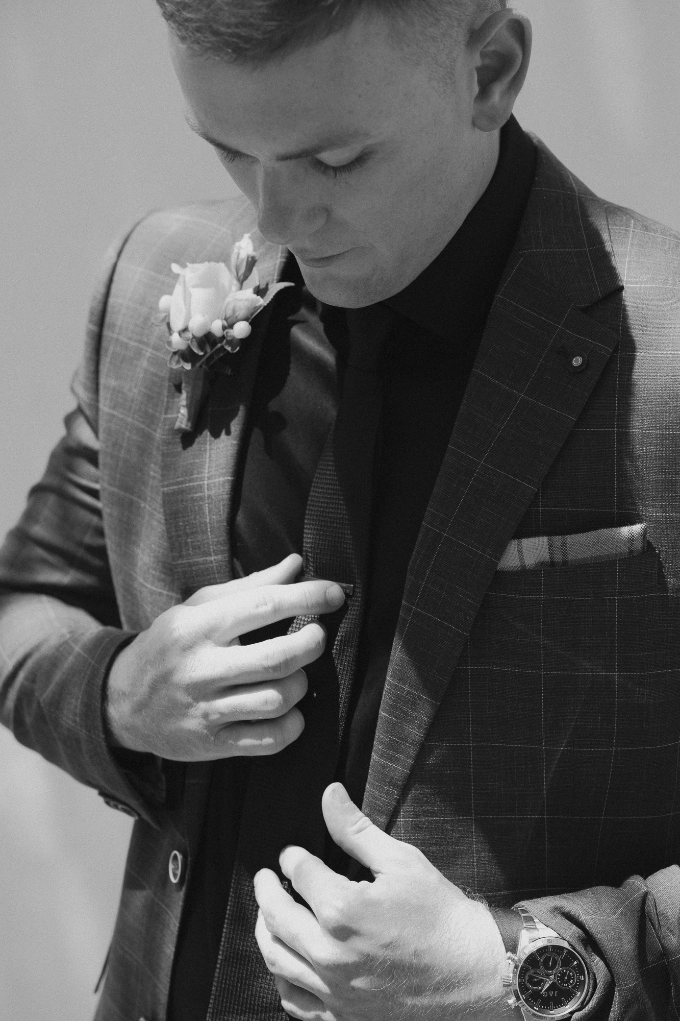 A man in a suit adjusting his jacket, wearing a wristwatch, with a boutonniere on his lapel, looking down. Amarti Wedding in Cowwarr