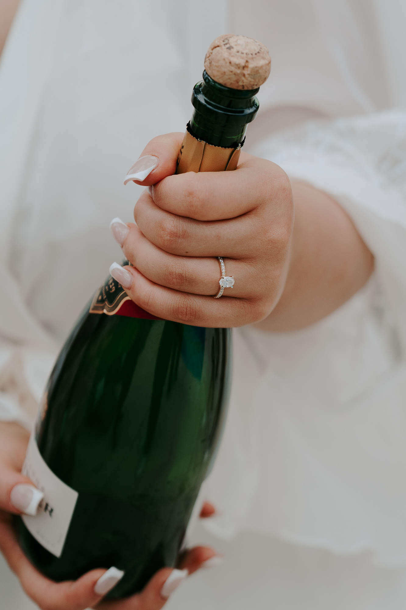Close-up of a hand with a diamond ring, holding a champagne bottle with a cork, ready to pop.