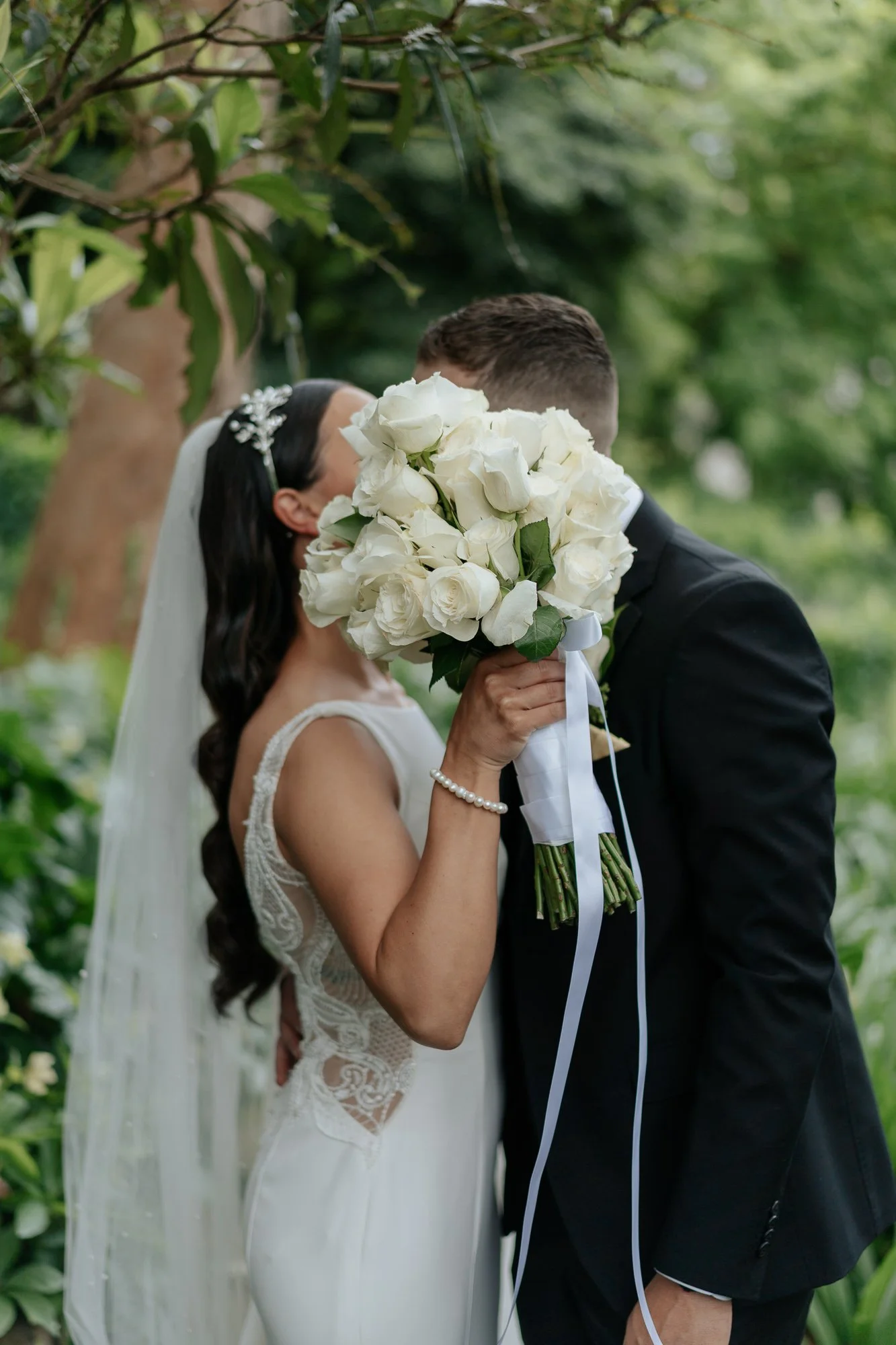 Bride and groom kissing outdoors at Leonda by the Yarra, the bride holding a large bouquet of white roses.