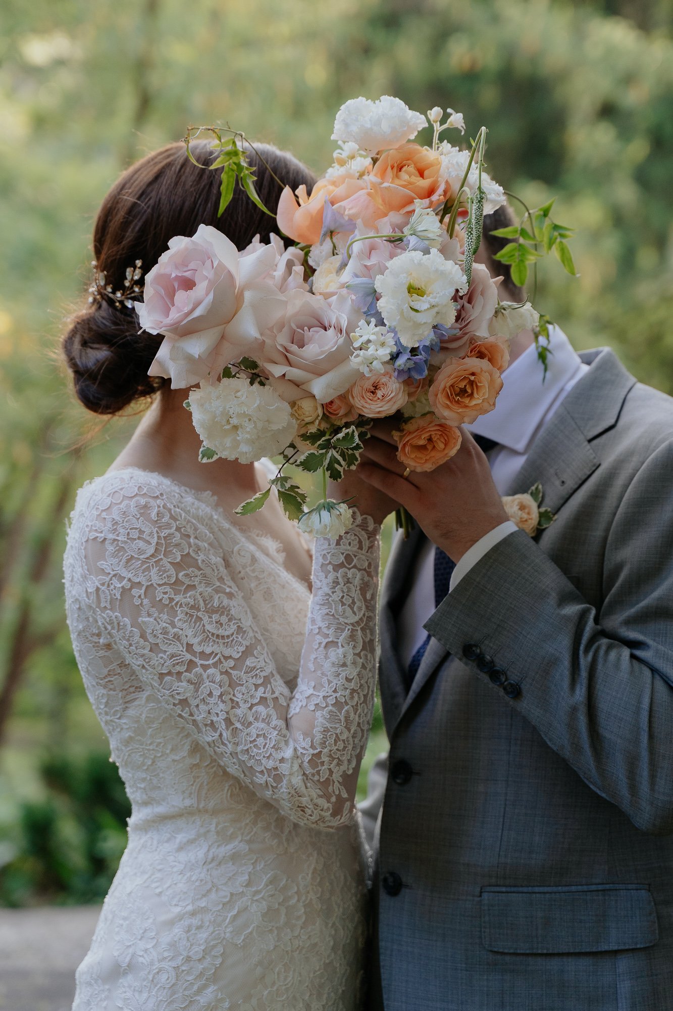 A bride and groom kissing behind a bouquet of flowers at their wedding.