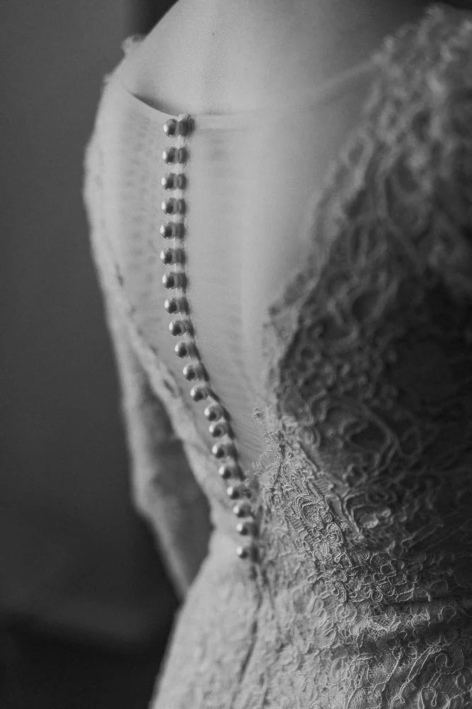 Melbourne Luxury Wedding Photography. Close-up view of a wedding dress with lace detail and pearl buttons running down the back.