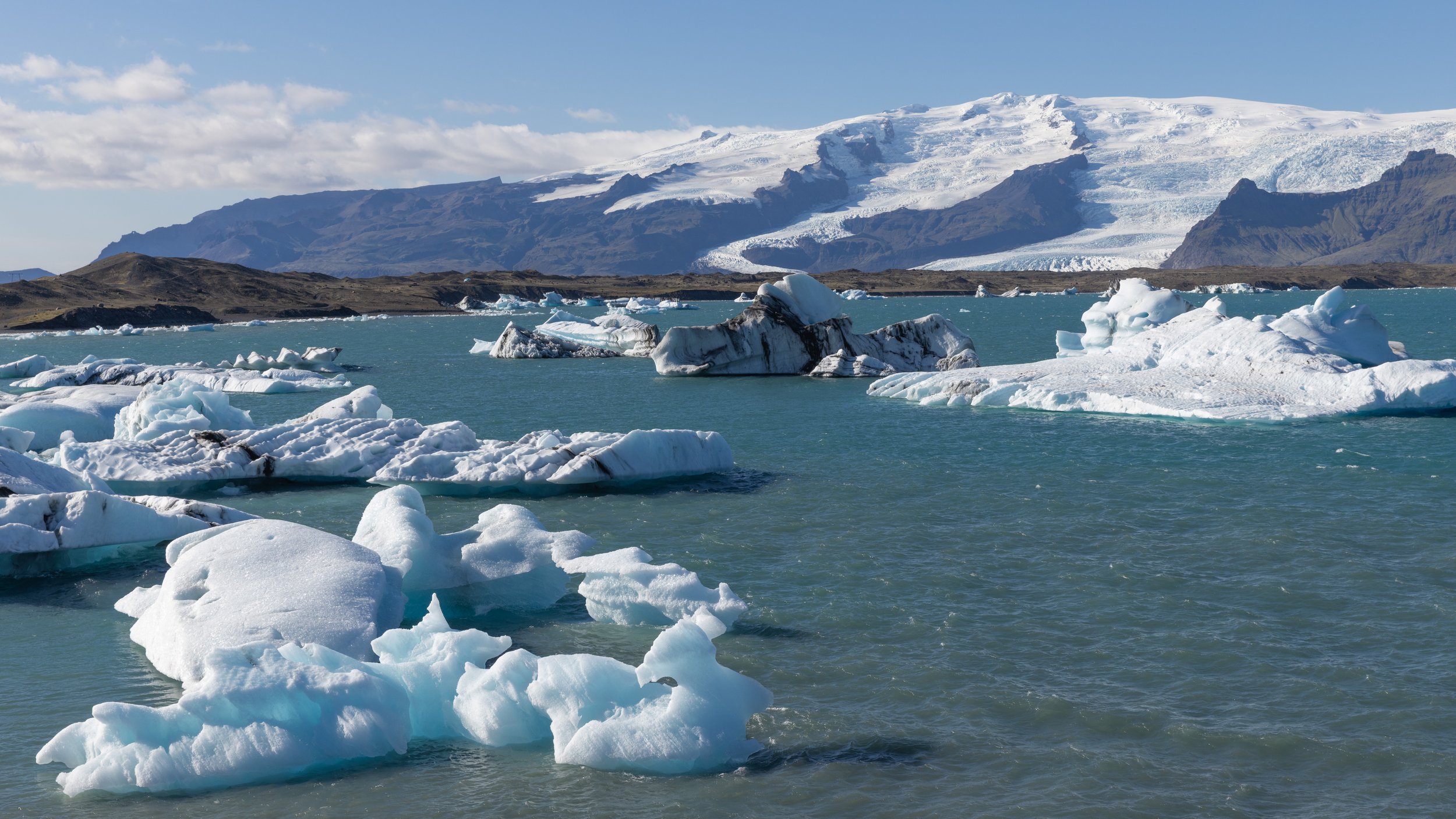 Icebergs floating in a cold ocean with snow-capped mountains in the background.