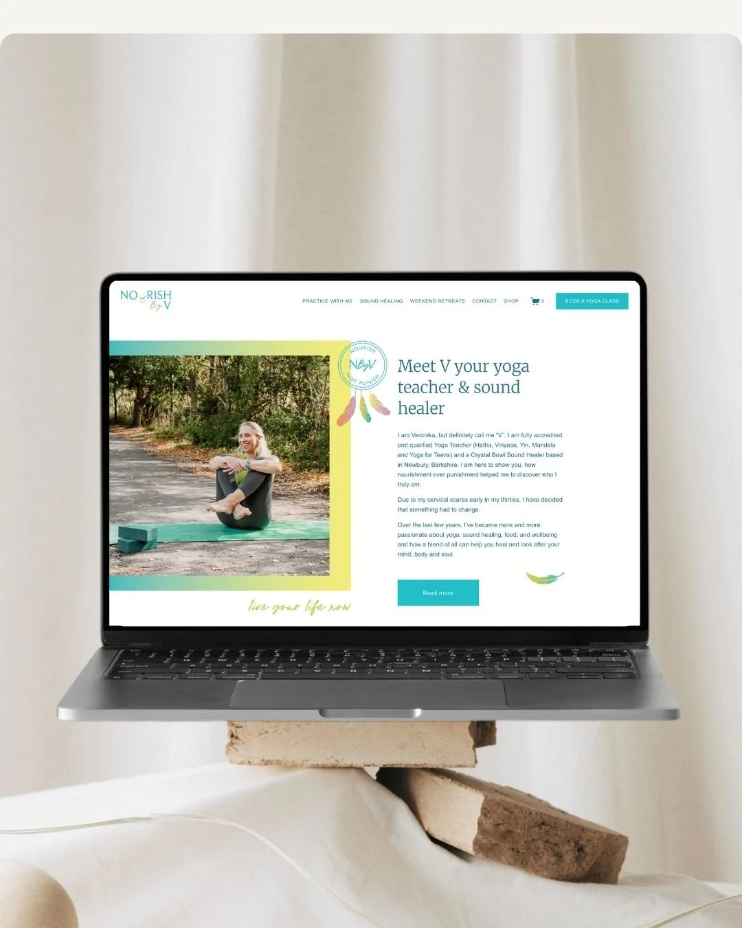 Laptop displaying a yoga website with a picture of a woman outdoors, text about yoga teacher and sound healer, and a 'Read more' button.