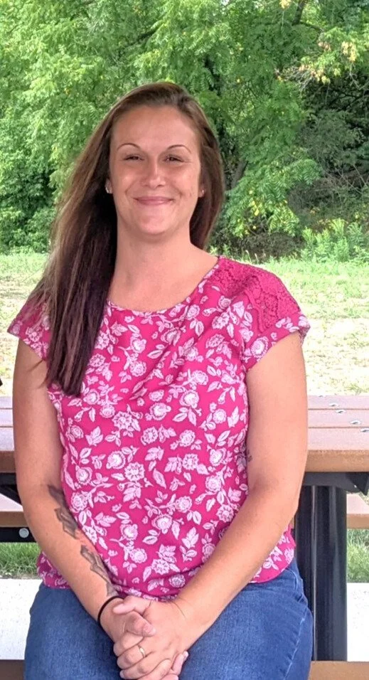 Person with glasses and brown hair wearing a pink shirt and black jacket