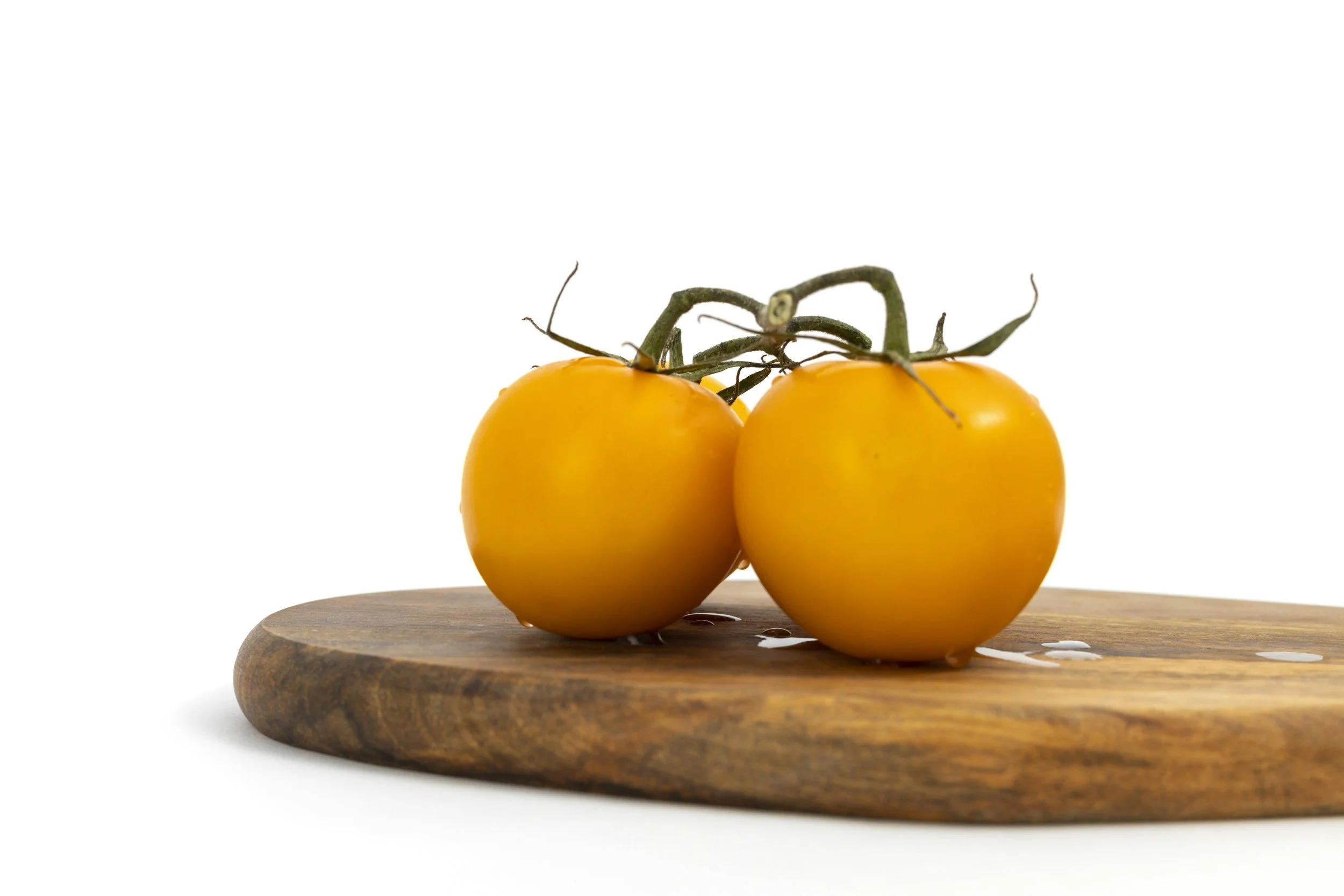 Two yellow cherry tomatoes on a wooden cutting board against a white background.