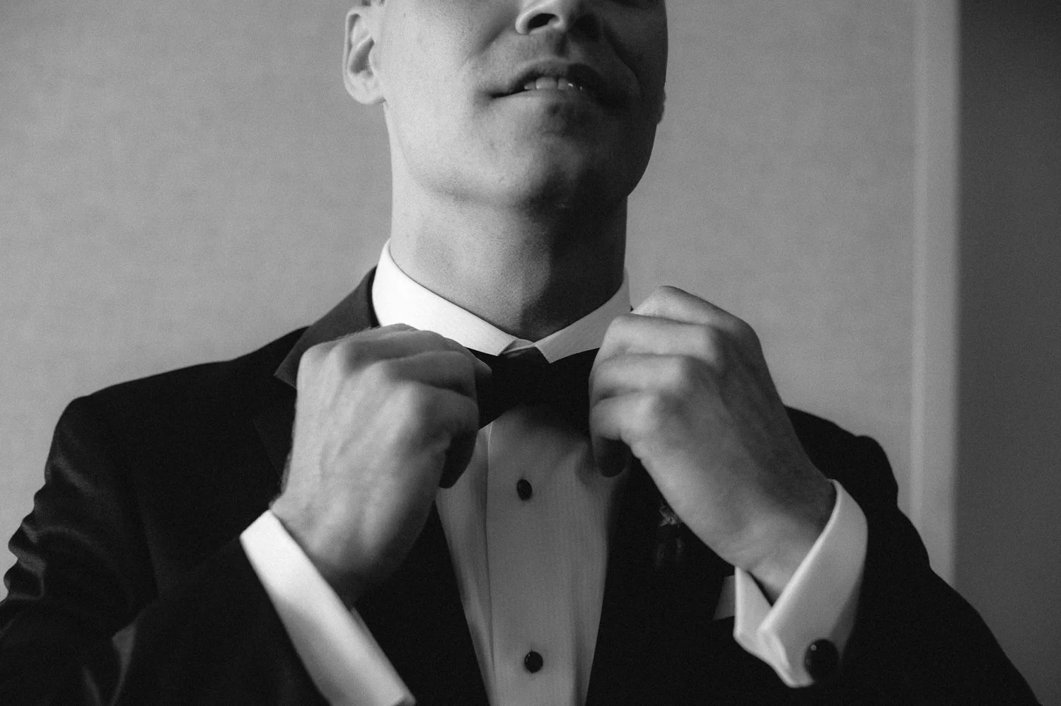 A dapper groom adjusting his bow-tie depicted in black and white photography.