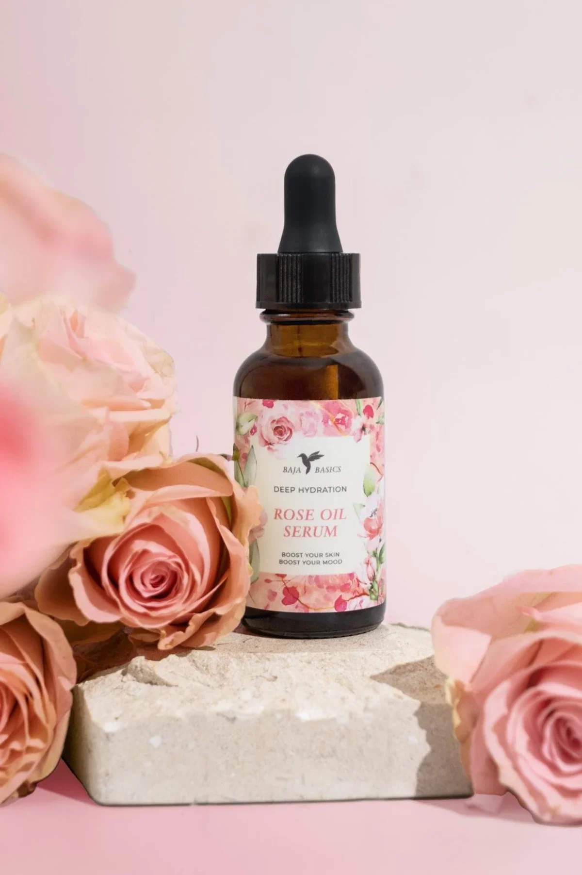 Skincare product photography of a serum bottle on stone block with pink roses and background. Photo for e-commerce, campaigns, and marketing.