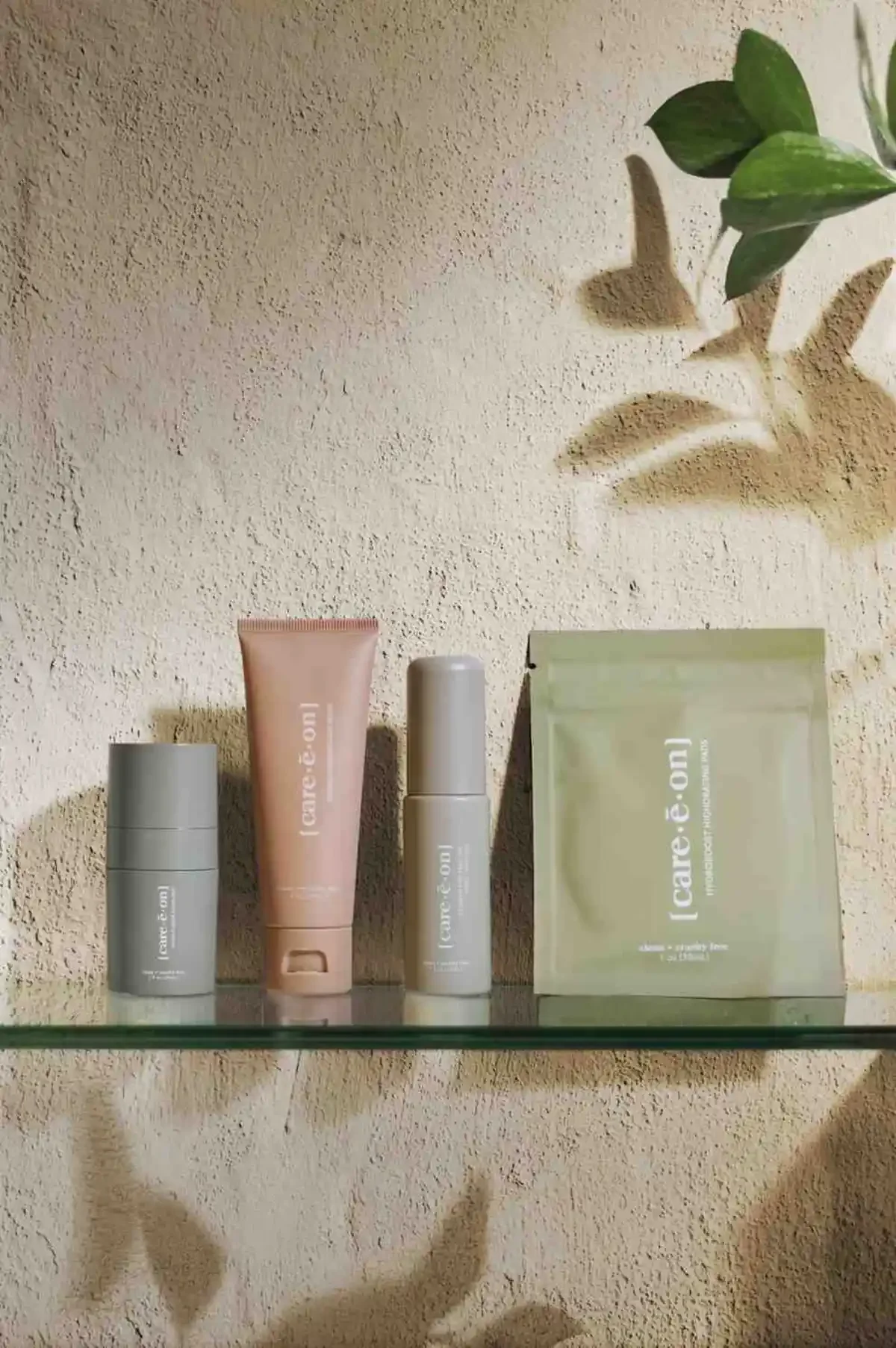 Skincare product photography of products on glass shelf with plants and textured beige wall. Photo for e-commerce, campaigns, and marketing.
