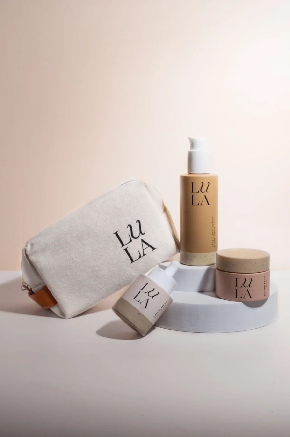 Skincare product photography of beige bottles and bag with white blocks and beige background. Photo content for e-commerce, campaigns, and marketing.