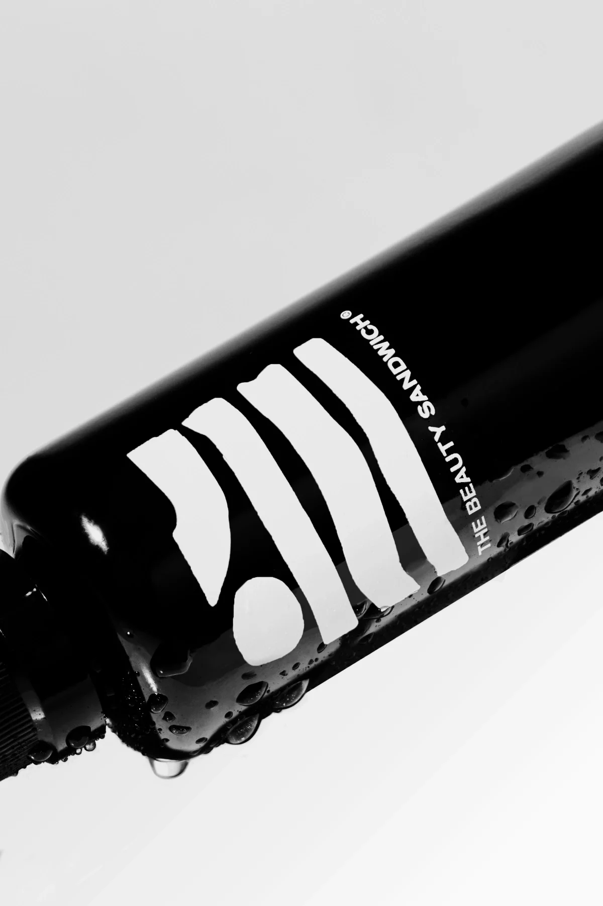 Professional skincare product photography of a glossy black skincare bottle captured at a dynamic angle, detailed with water droplets to emphasize hydration and texture. Shot on a clean, minimal background, this style highlights packaging design and 