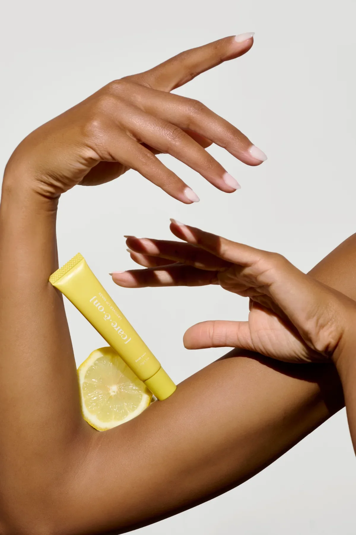 Beauty product photography of arms and hands with yellow lip balm and lemon slice balanced on arm. Photo for e-commerce, campaigns, and marketing.