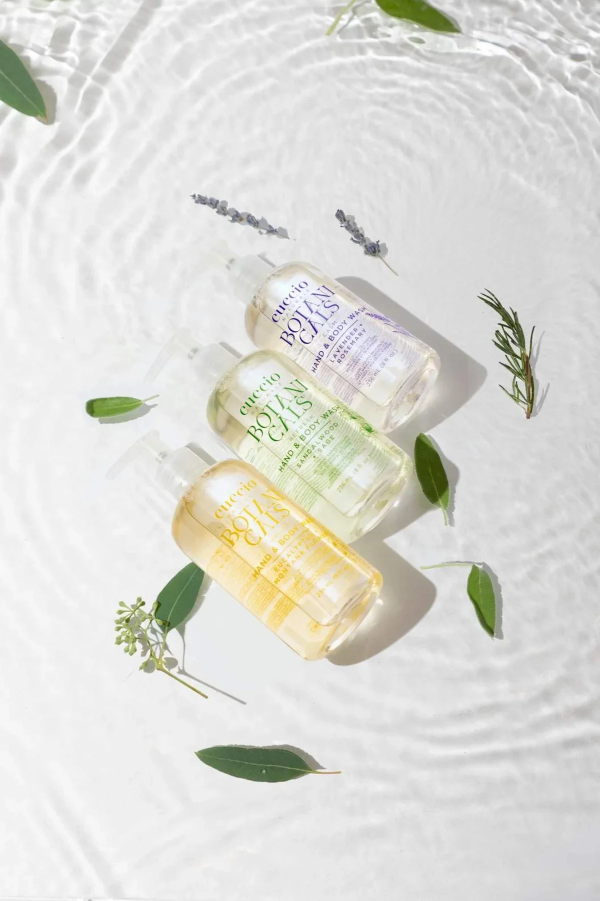Bodycare product photography of three bottles in a row on swirling water with small leaves. Photo for e-commerce, campaigns, and marketing.