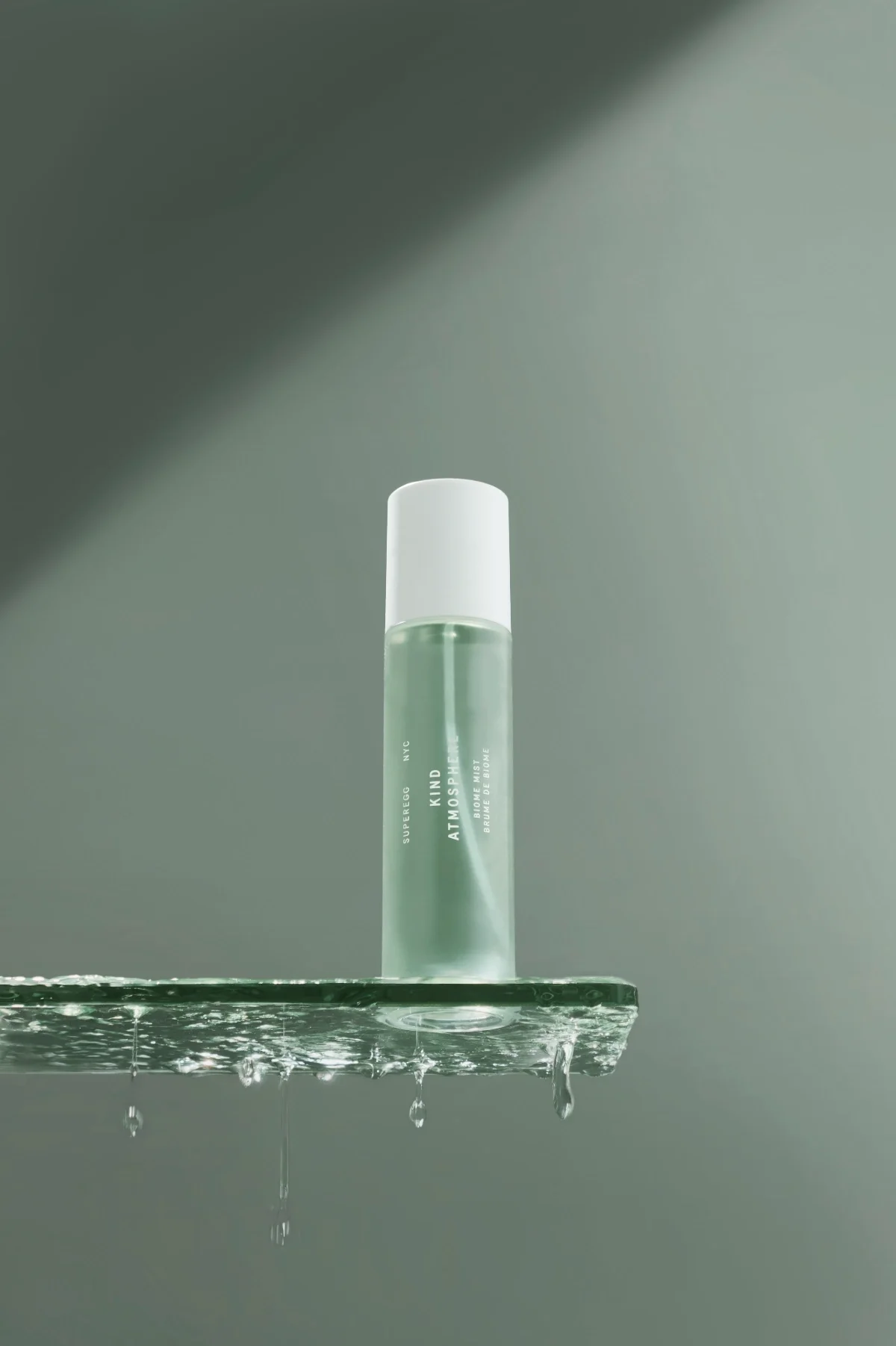 Luxury skincare mist bottle on glass shelf with water droplets, minimal green aesthetic, high-end beauty product photography