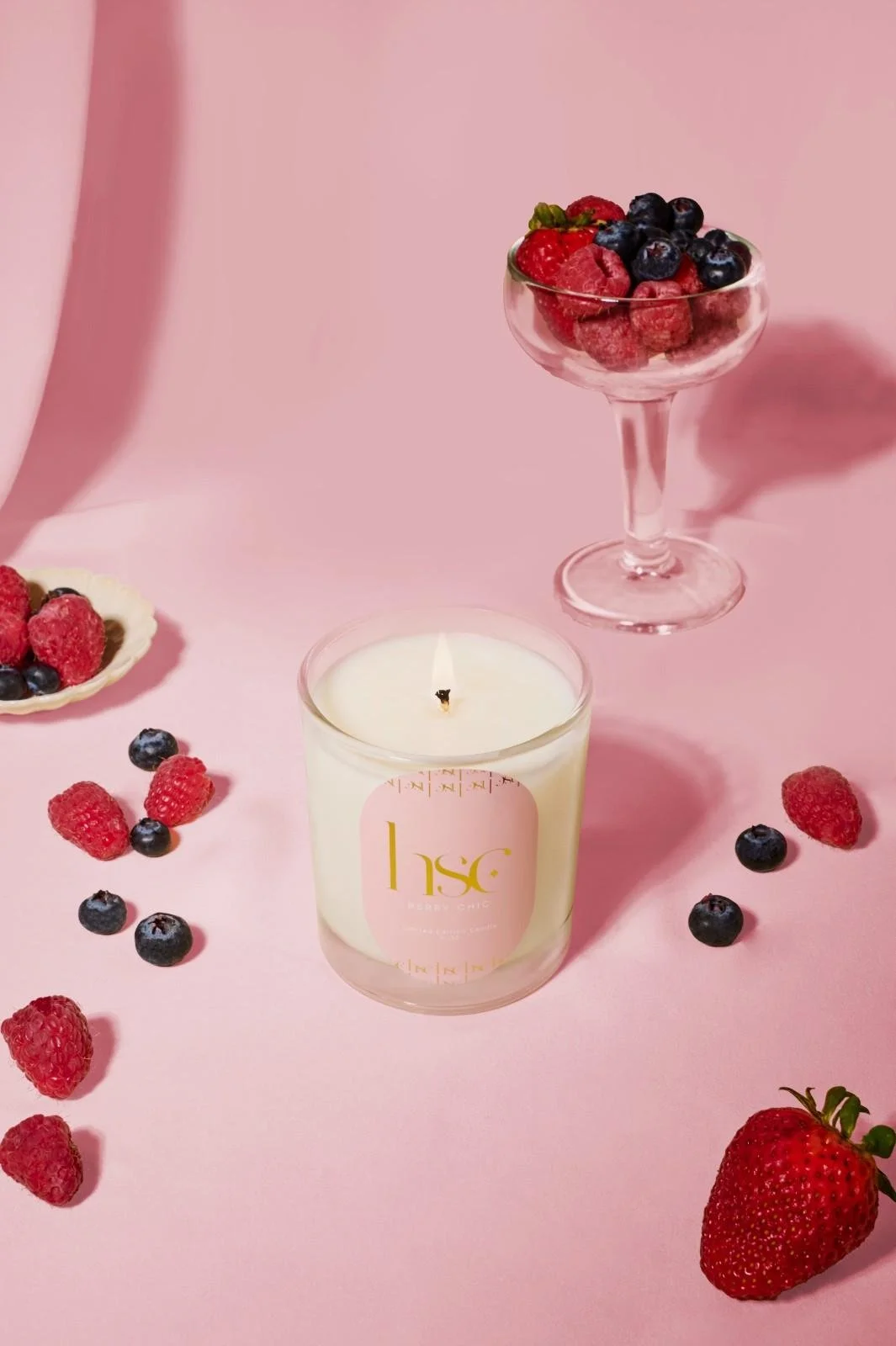 Seattle candle product photography of a white candle on a pink background surrounded by fresh raspberries, strawberries, and blueberries