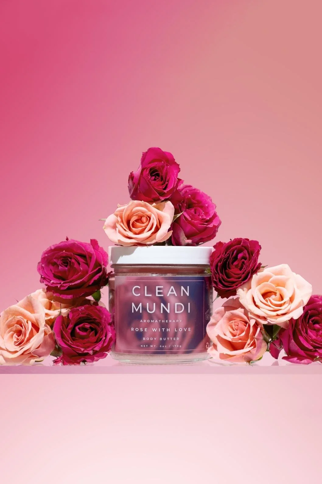 Skincare product photography of a rose body butter surrounded by various pink and red roses and a gradient pink background