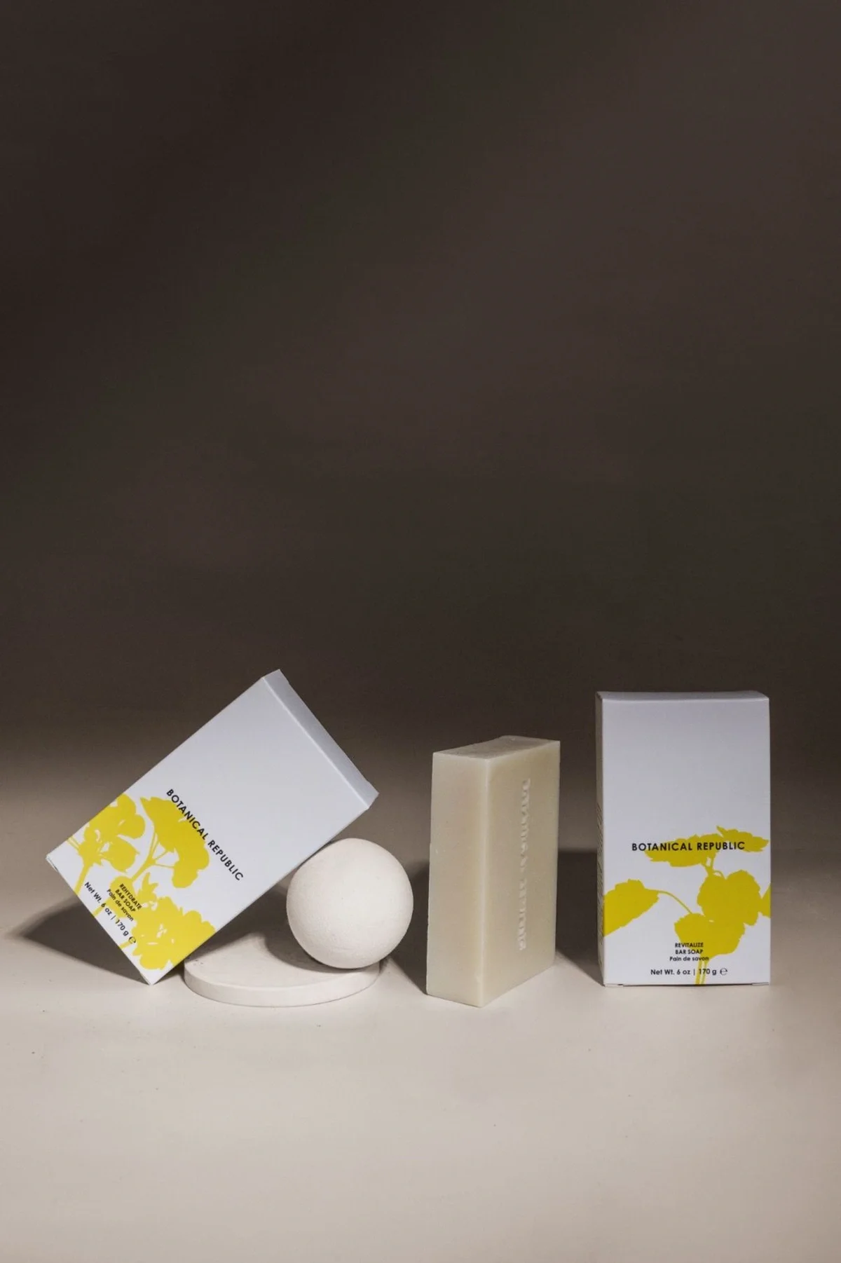 Skincare product photography of a few soap bars placed in a row, with one of the bars leaning against a ball and a dark brown gradient background