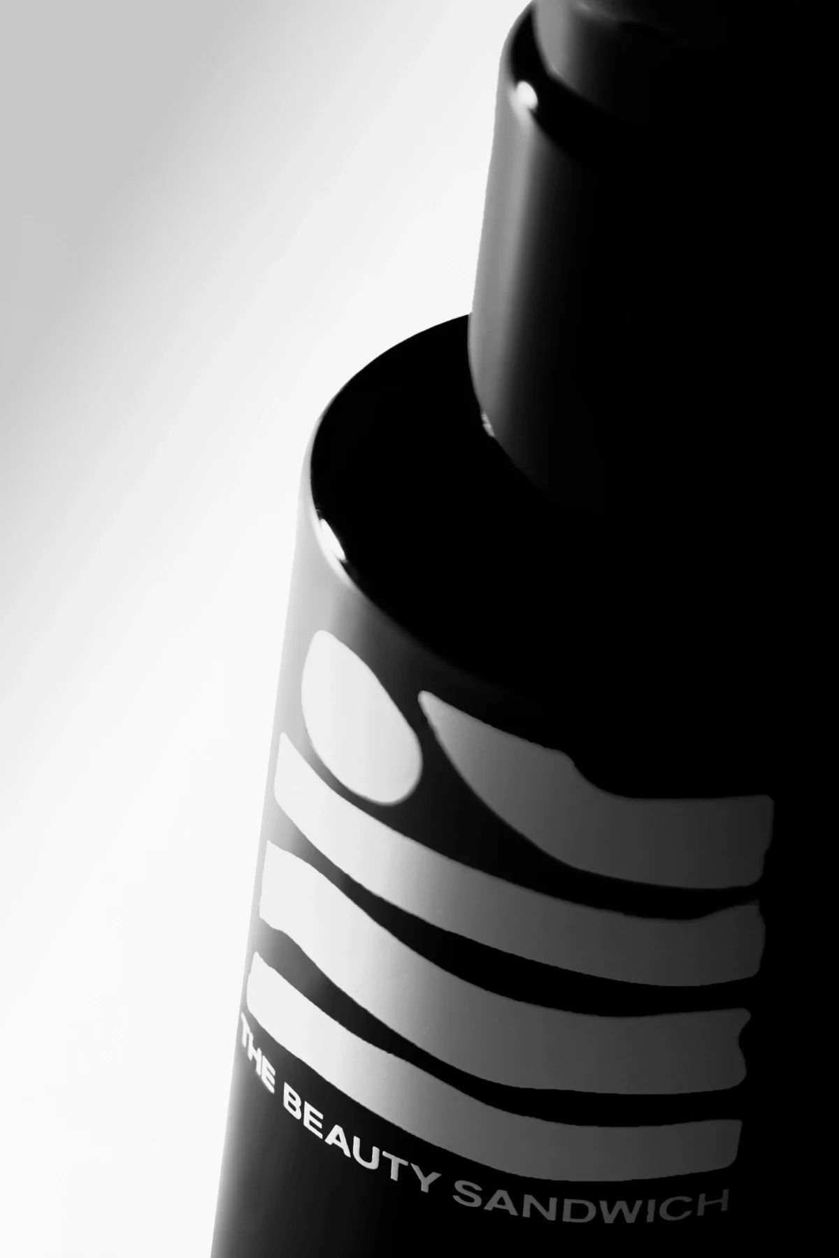Close-up skincare product photography of a sleek black serum bottle with a minimalist label, captured in high-contrast lighting against a clean background. This composition emphasizes form, texture, and premium packaging—ideal for beauty brands seeki