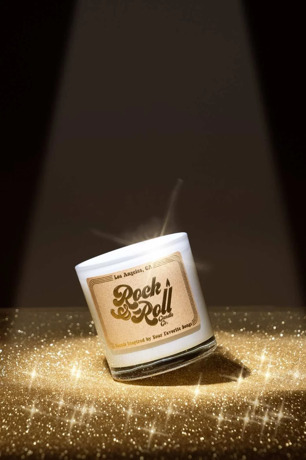 Seattle product photography of a candle tilting on a gold glittering tabletop with a dark background and spotlight on the candle