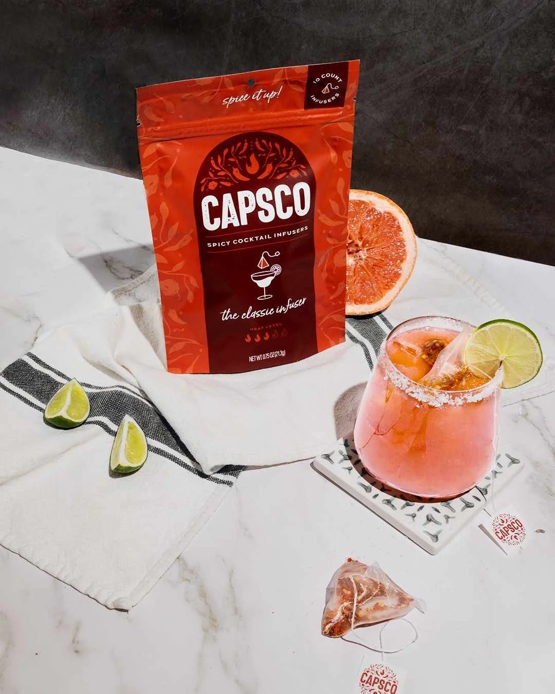 Food product photography of a cocktail mix pouch set on top of a kitchen towel next to a fresh margarita drink