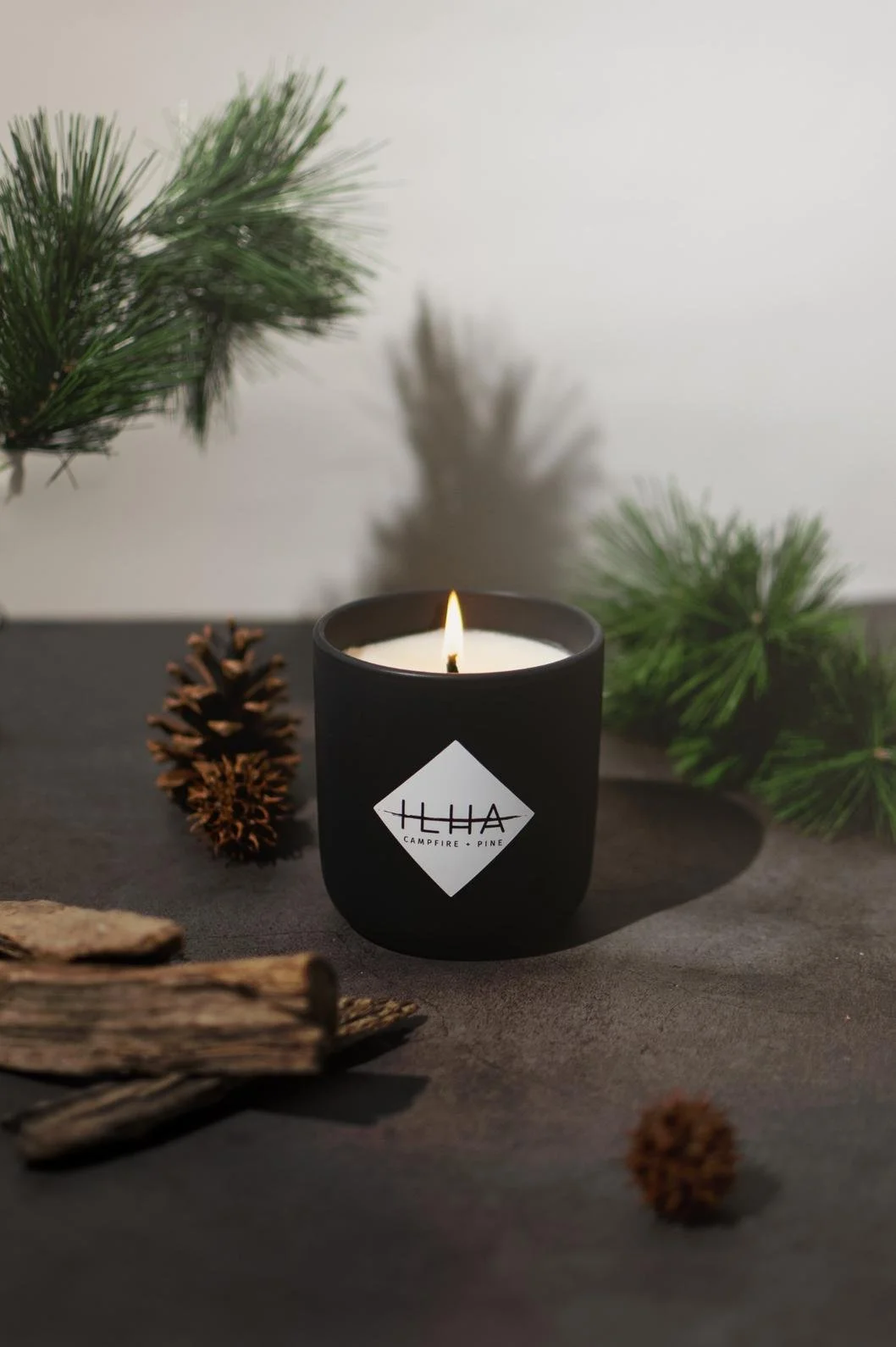 Seattle candle product photography of a black candle surrounded by pinecones, fir cuttings, and pieces of wood