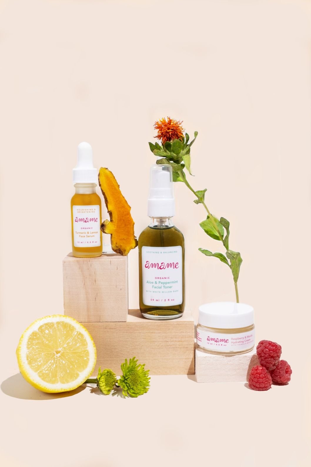 Skincare product photography of serums, creams, and facial oils placed on various wooden blocks and surrounded by flower and fresh ingredients such as lemons and raspberries