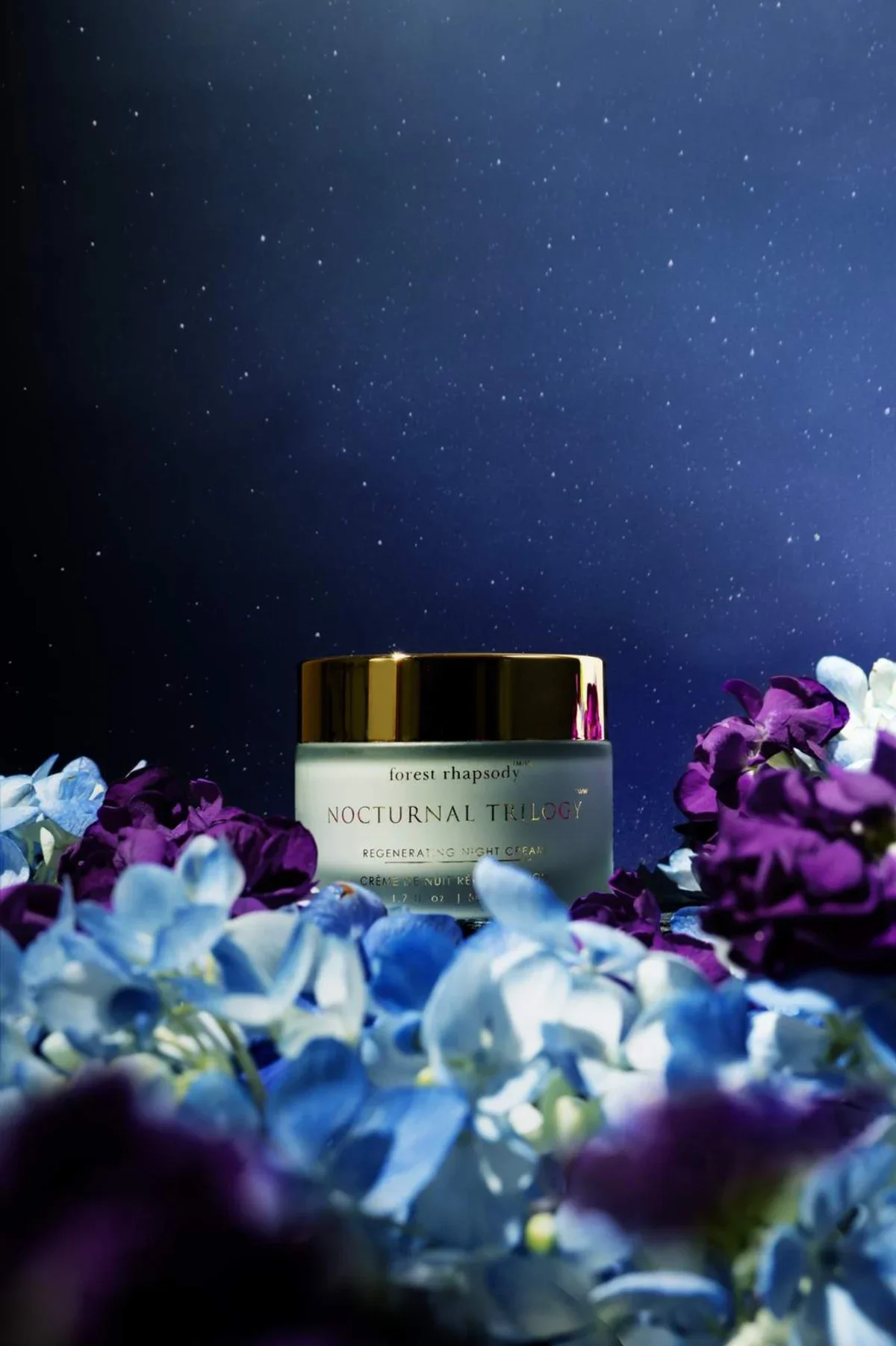 Skincare product photography of a night cream in a blue and purple floral field with a moody night sky lit with stars