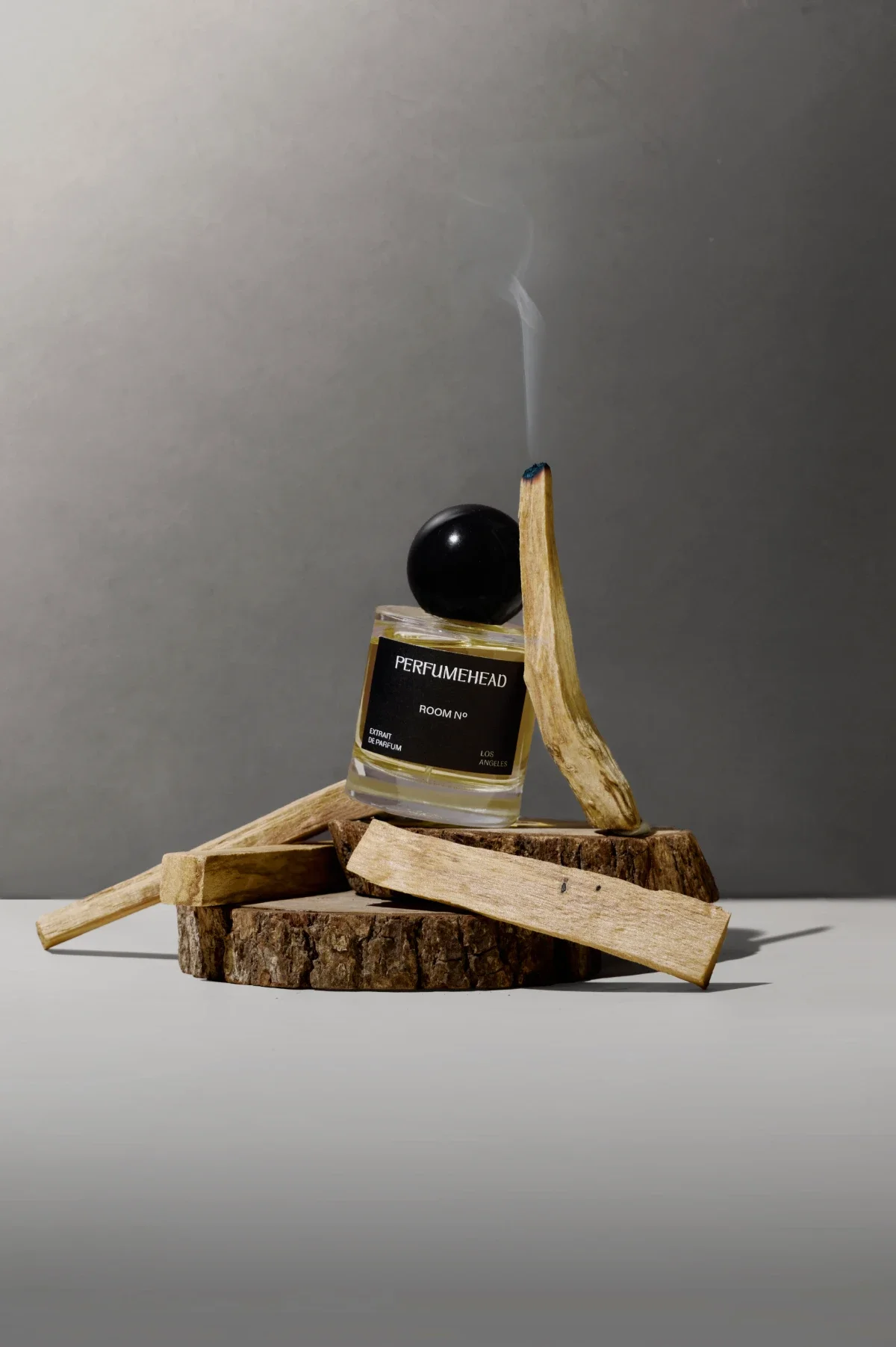 Luxury perfume product photography of bottle and palo santo, wood, and grey gradient background. Photo for e-commerce, campaigns, and marketing.