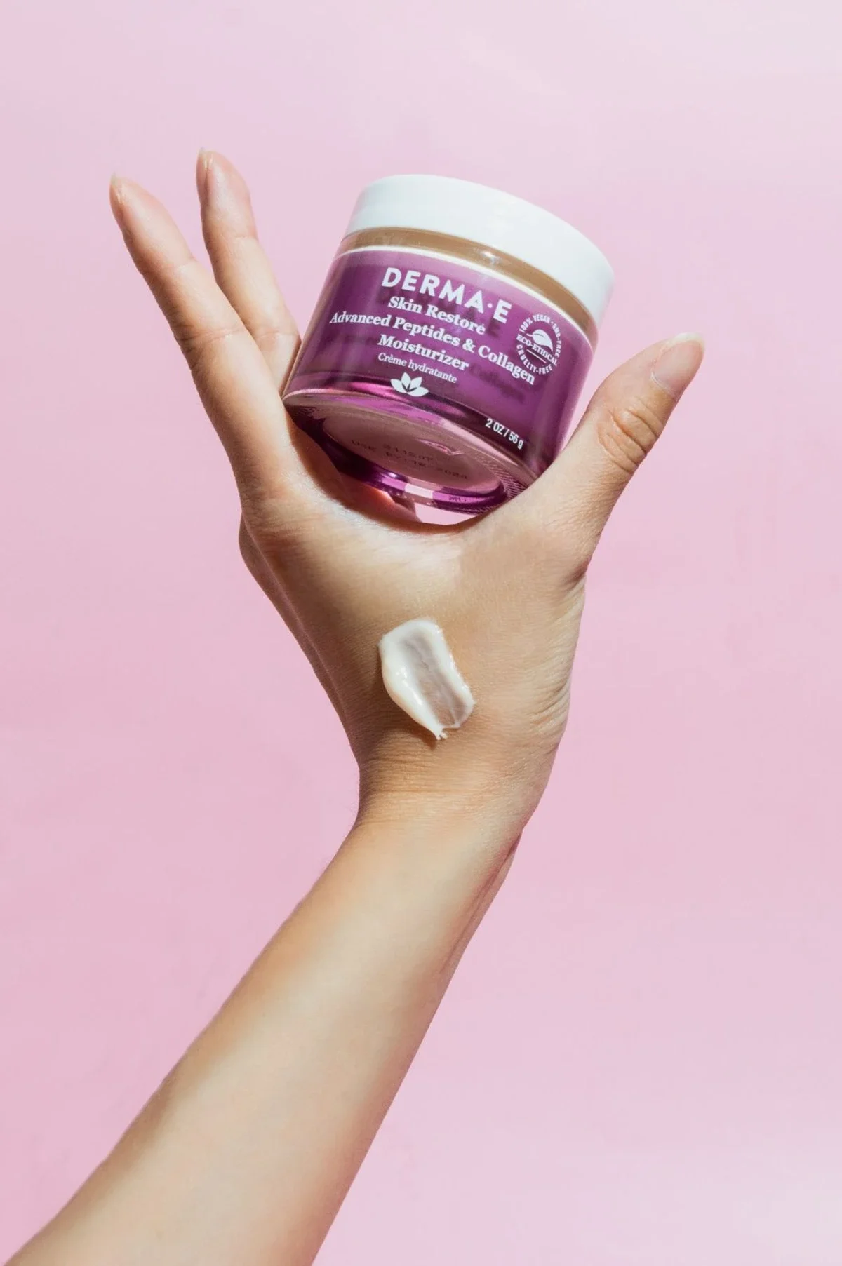 Skincare product photography of a hand with  cream smear holding a purple jar with pink background. Photo for e-commerce, campaign, and marketing.