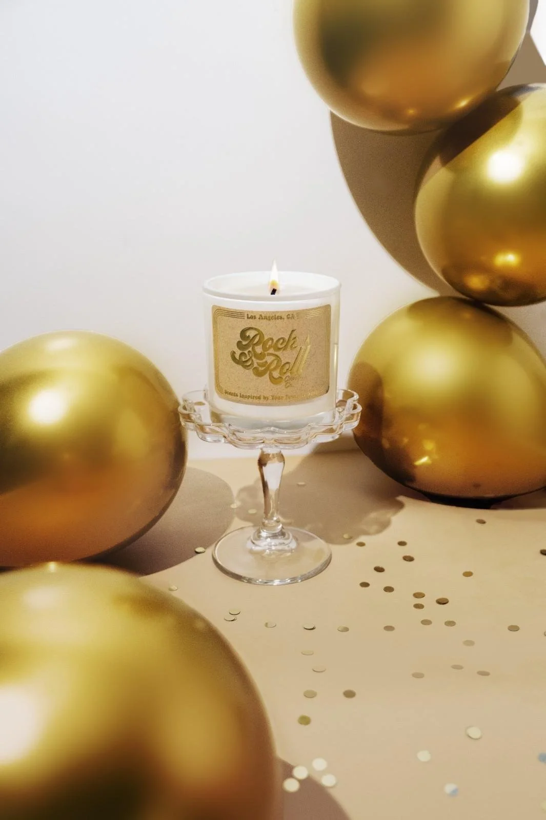 Seattle candle product photography of a white candle on a glass pedestal surrounded by gold balloons and gold glitter