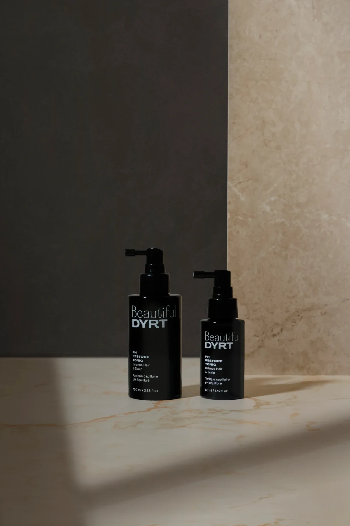Haircare serum product photography of two black bottles with stone and grey background, shadows. Photo for e-commerce, campaigns, and marketing.