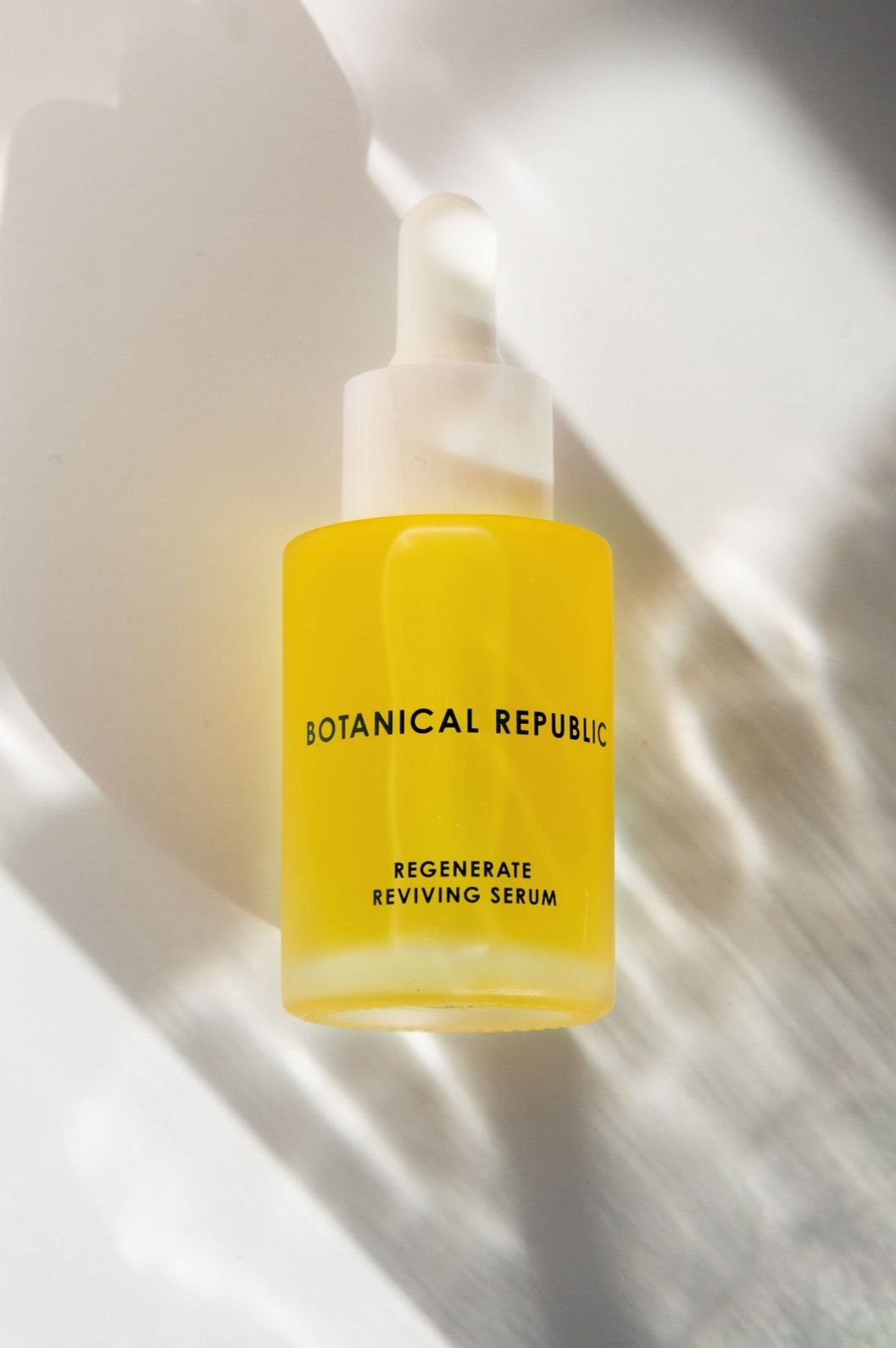 Skincare product photography of a serum bottle with scattered dappled shadows and warm sunny lighting