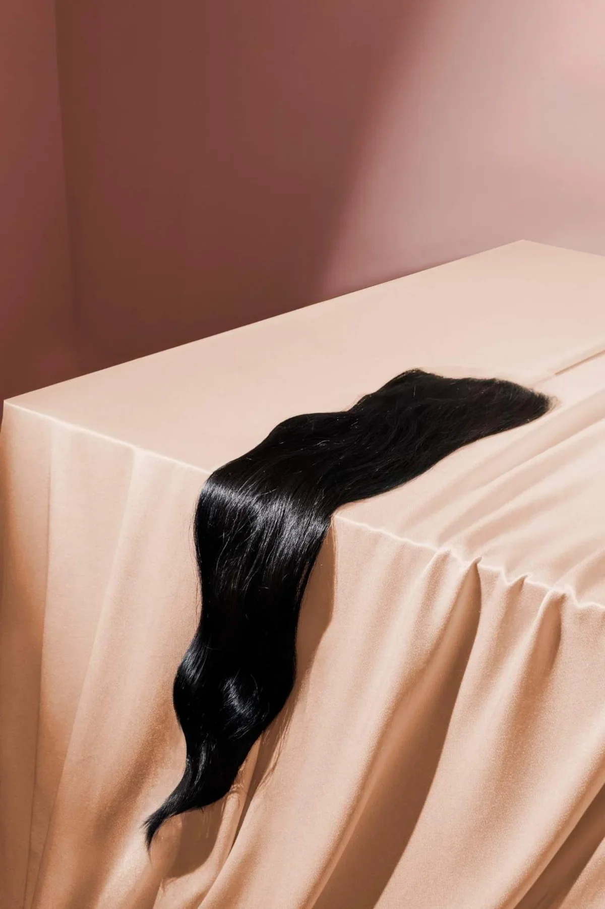 Hair product photography of an extension bundle laid on top of pink satin fabric with dramatic shadows in the background