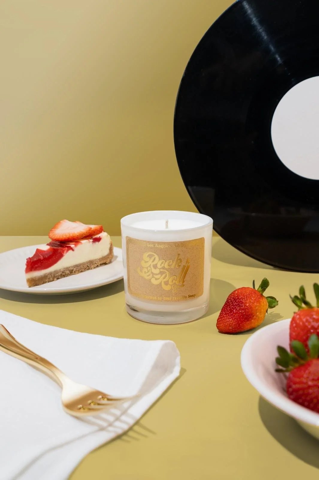Seattle candle product photography of a white candle surrounded by plates of strawberries and cake on a golden beige background