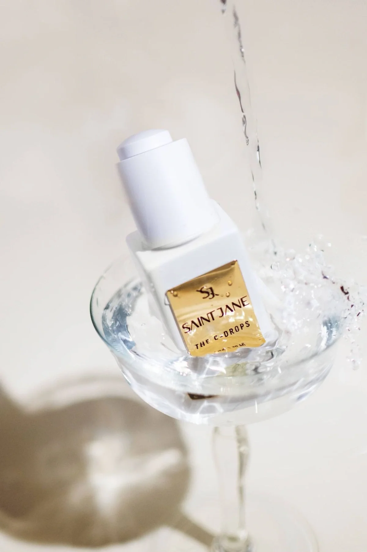 Skincare product photography of serum bottle splashing into glass of water. Photo content for e-commerce, campaigns, and marketing.