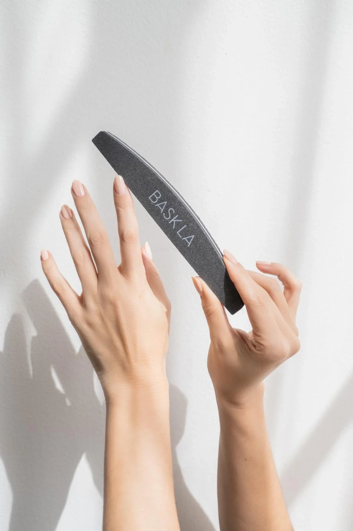 Nailcare product photography with hands, the right hand holds nail file with a dappled background. Photo for e-commerce, campaign, and marketing.