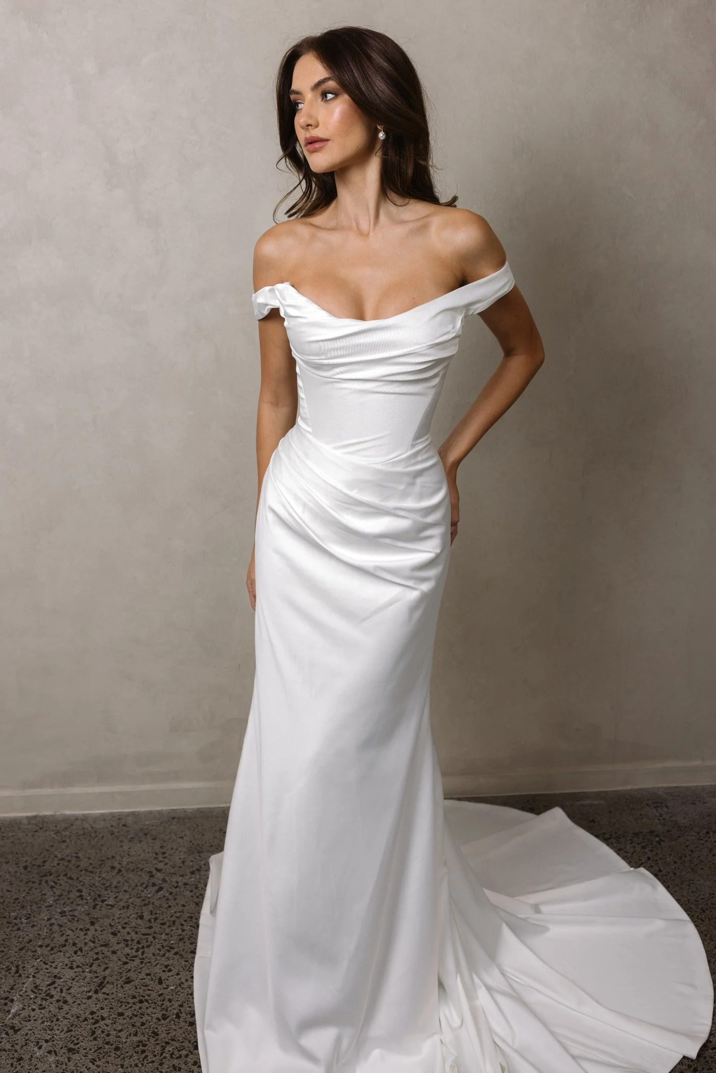 Lydia by Trish Peng satin wedding dress featuring a soft off-the-shoulder neckline, draped bodice, sculpted basque waist and fitted ruched skirt, available at Spellbound Bridal Ireland.