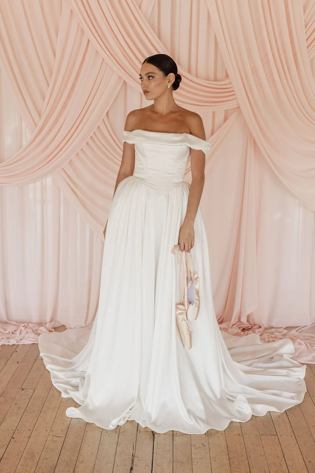 Diana by Trish Peng off-white satin wedding dress with a draped off-the-shoulder neckline, structured basque waist, A-line skirt and detachable bustle, available at Spellbound Bridal Ireland.